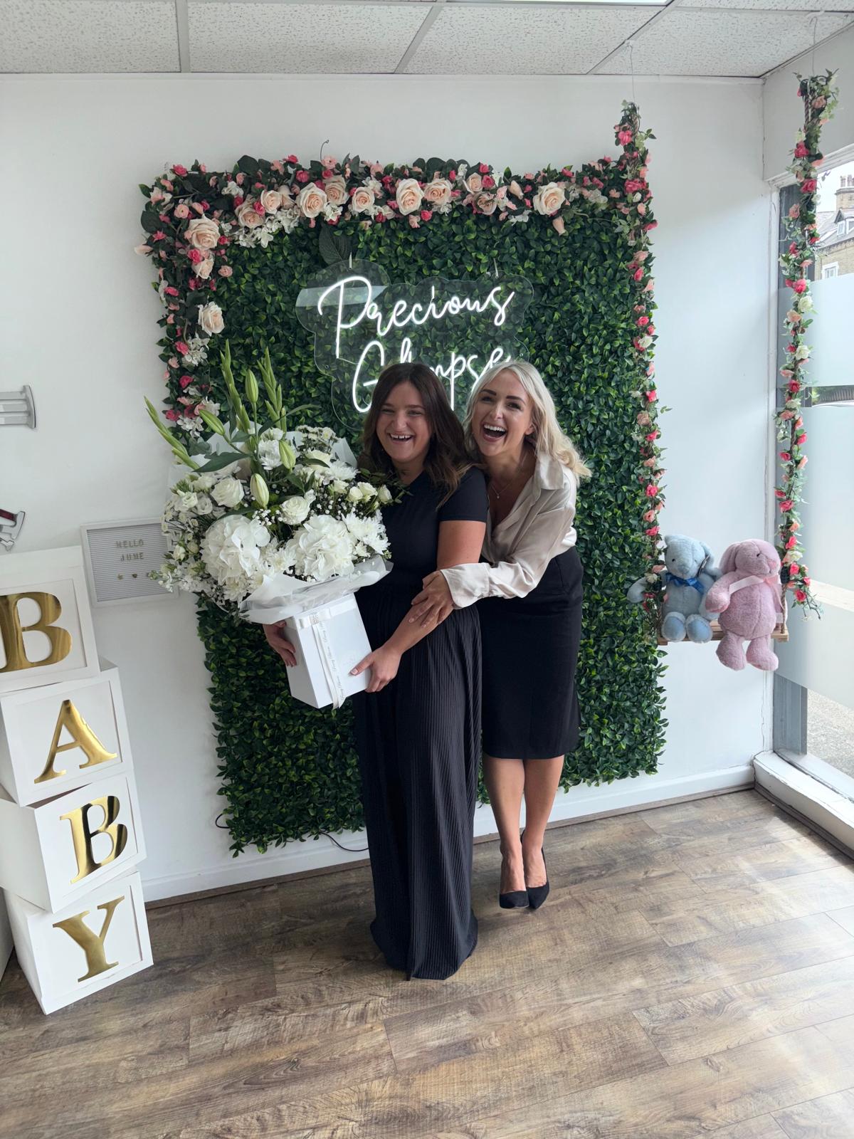 Two women laughing together at the Precious Glimpse flower wall