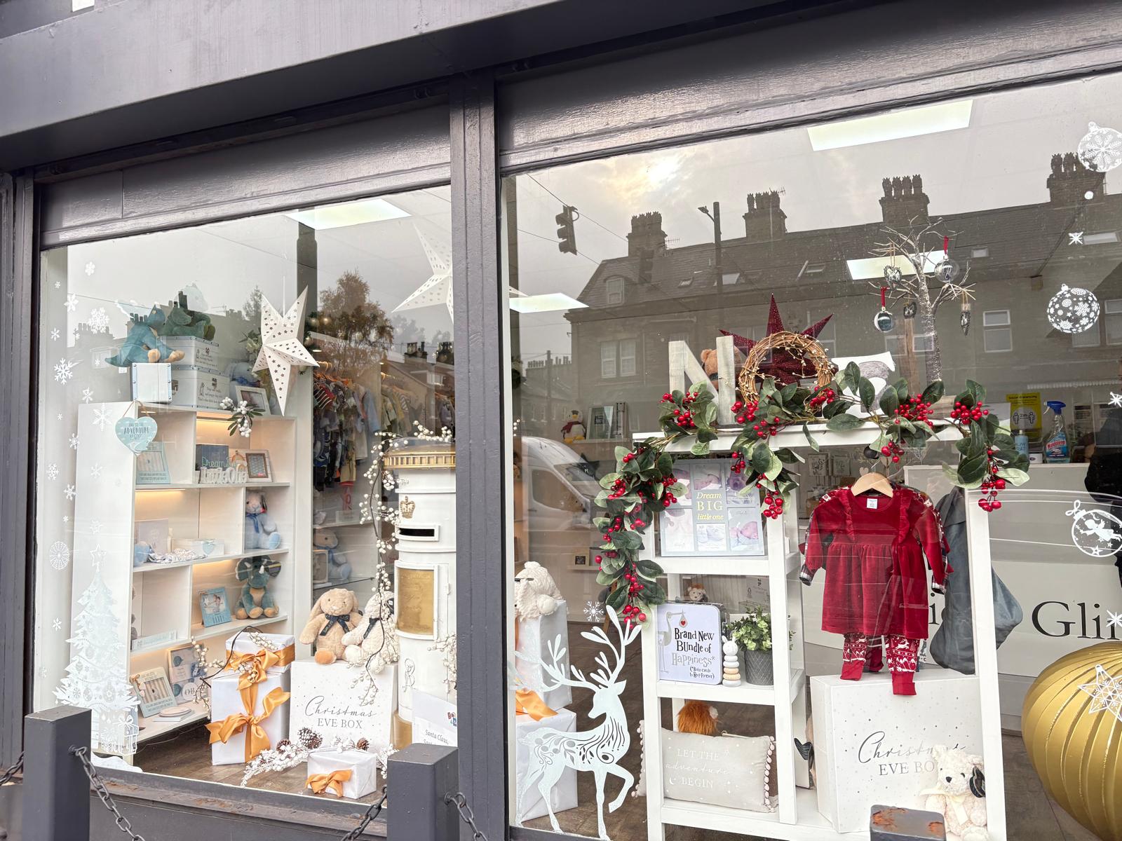 The Precious Glimpse window dressed for Christmas, with garlands, gift boxes and a red baby dress