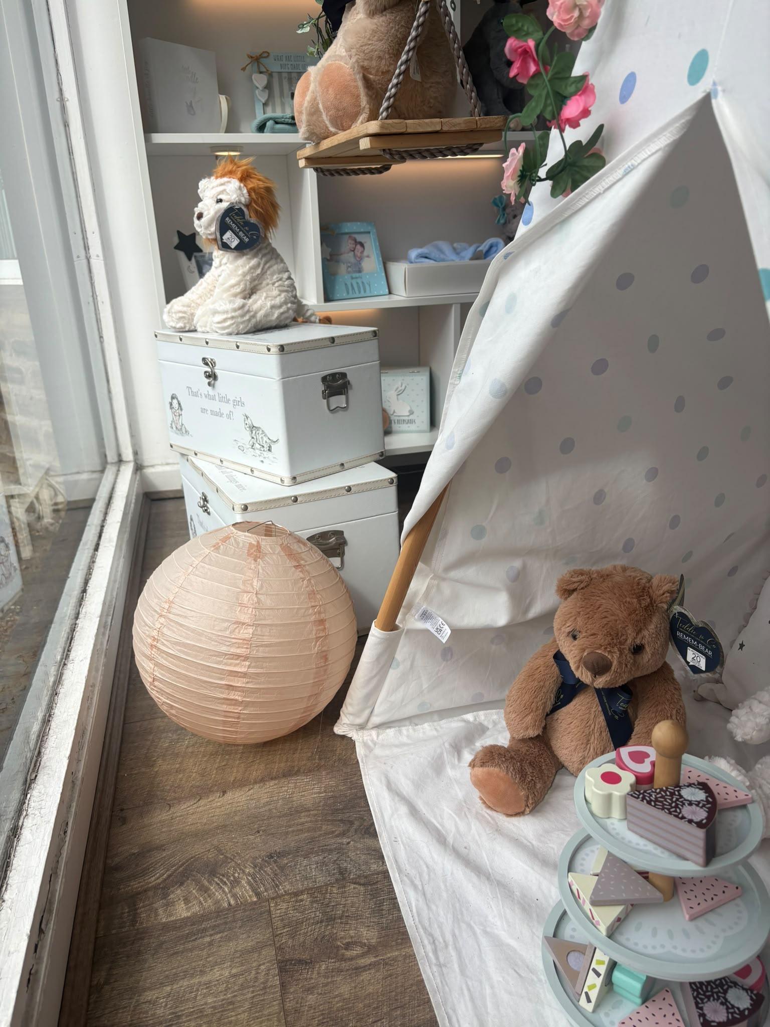 A teddy sitting in a play tent beside keepsake boxes in the Precious Glimpse window display