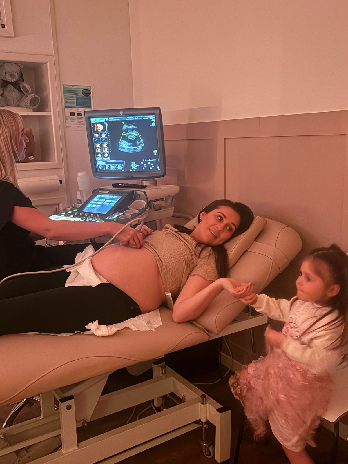A sonographer scanning an expectant mum while her daughter holds her hand